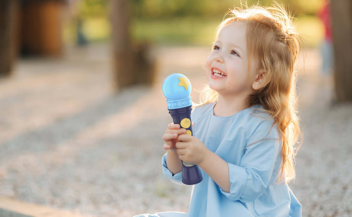 Child smiling and holding Bluey karaoke microphone toy in a park