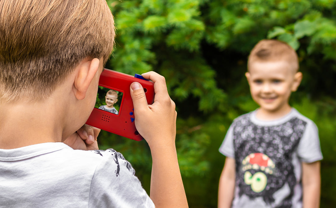 Boy using Spidey And His Amazing Friends Digital Camera to take a photo of another smiling boy outdoors