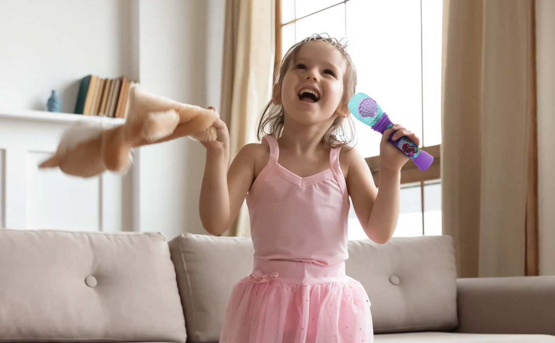 Young girl singing with Ariel karaoke microphone toy while playing in the living room